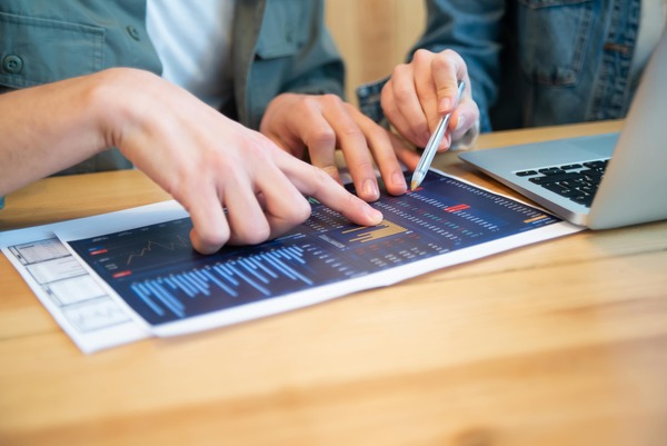 Hands pointing at a printed market report beside a laptop