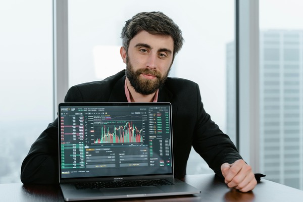 Man at an office desk with a laptop showing trading charts