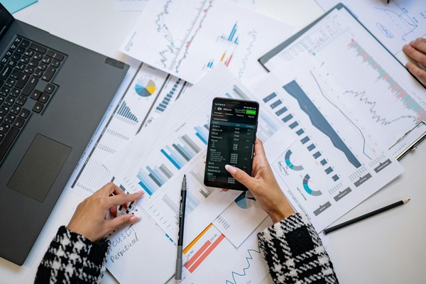 Person checking a phone over printed financial charts