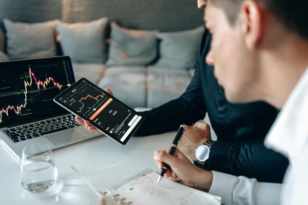 Two people reviewing a market chart on a tablet and laptop